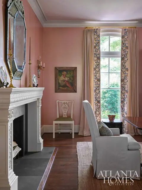 Pink living room with ornate fireplace, antique chair, and floral curtains.