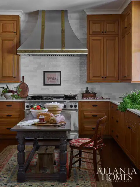 Warm wood kitchen with stainless steel range, decorative hood, and rustic table with bread.