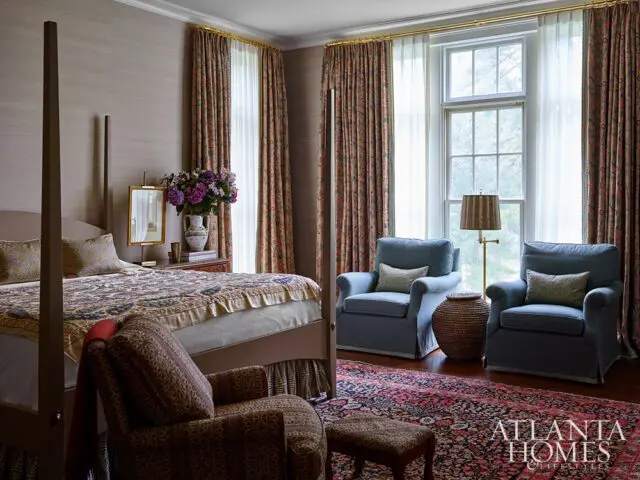 Bedroom with four-poster bed, blue armchairs, patterned rug, and floral curtains.