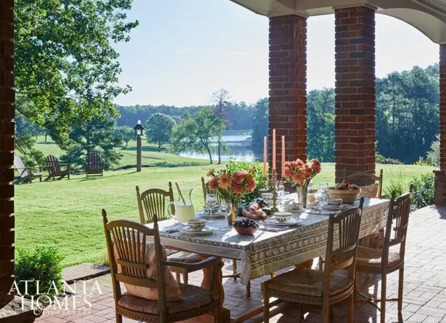 Covered porch with dining table set for a meal, overlooking a lake and lawn.