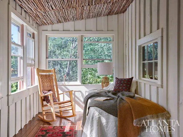 Bedroom with wood plank walls, twig ceiling, rocking chair, and bed with orange throw blanket.
