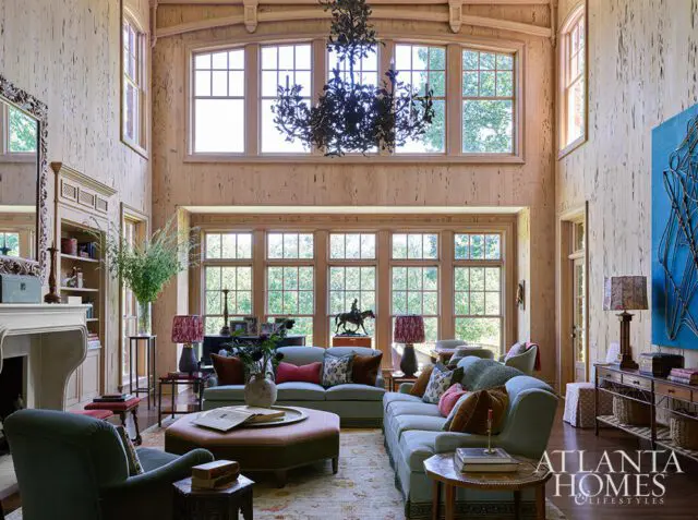 Living room with light blue sofas, wood paneled walls, large windows, and a dark chandelier.