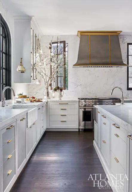 White kitchen with marble countertops, brass hardware, and stainless steel range.