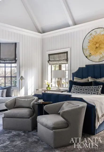 Bedroom with navy blue upholstered bed, two grey armchairs, and sunburst wall art.