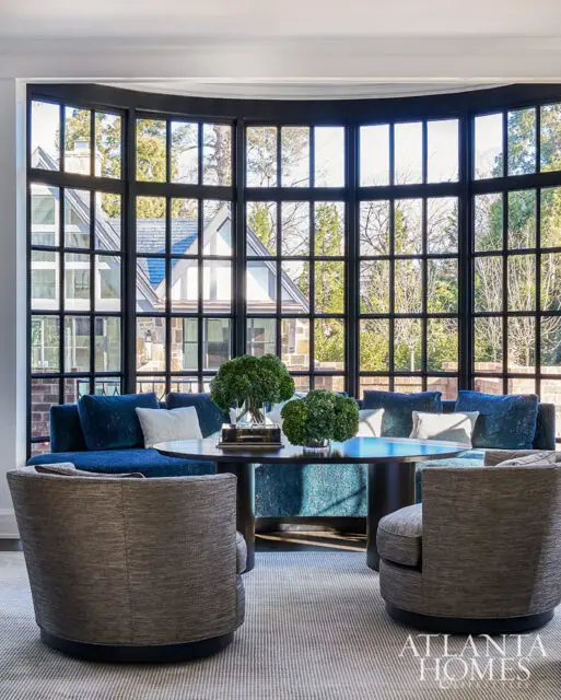 Living room with blue sectional, round table, and gray swivel chairs by large bay window