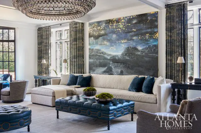 Living room with sectional sofa, blue tufted ottoman, and large abstract landscape painting.