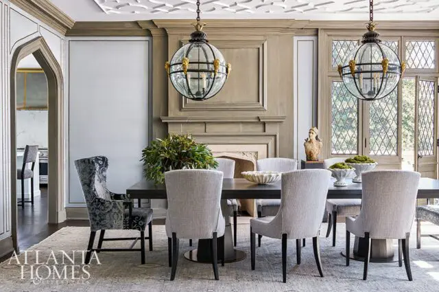 Dining room with gray upholstered chairs, dark wood table, fireplace, and ornate globe chandeliers.