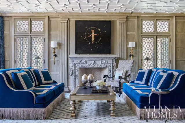 Living room with two blue velvet sofas, ornate fireplace, and artwork above the mantle.