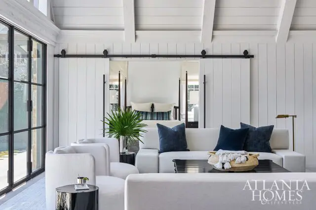 White living room with white sofas, navy pillows, black coffee table, and barn doors opening to a