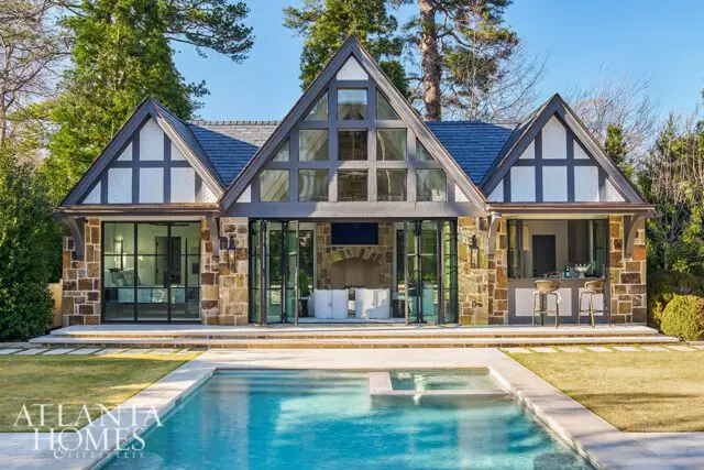 Tudor-style home with stone facade, large windows, and a swimming pool.