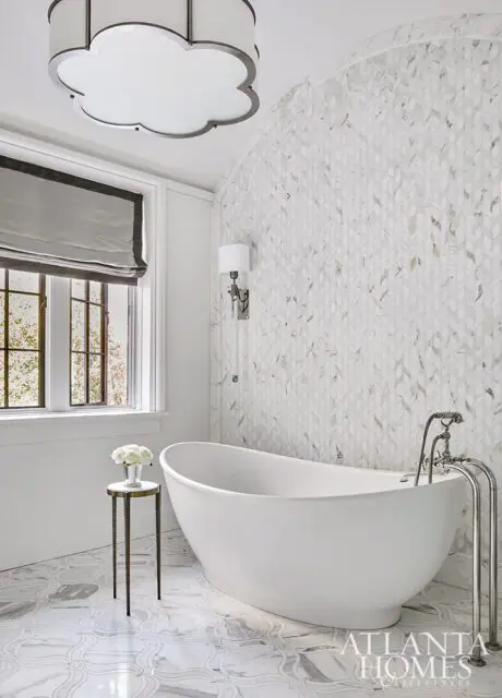 Freestanding white bathtub with marble leaf-patterned wall and ornate floor tile