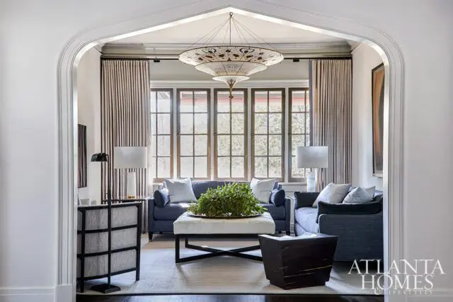 Living room with blue sofas, white ottoman with plant, and large ornate chandelier.
