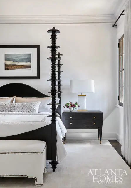 Black four-poster bed with white bedding, ornate black nightstand, and framed art.