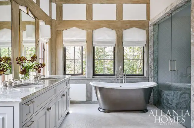 Bathroom with gray double vanity, freestanding tub, and glass shower with marble accents.