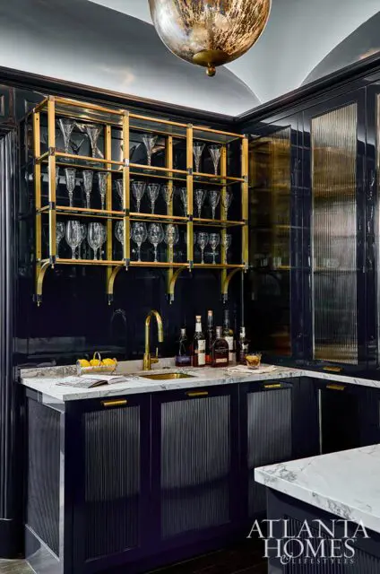 Dark blue bar with marble countertop, brass faucet, and gold shelving displaying glassware.