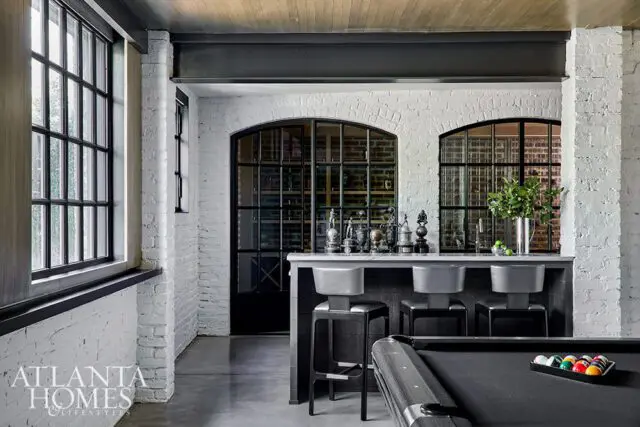 Bar area with white brick walls, marble countertop, and three bar stools. Pool table in foreground.