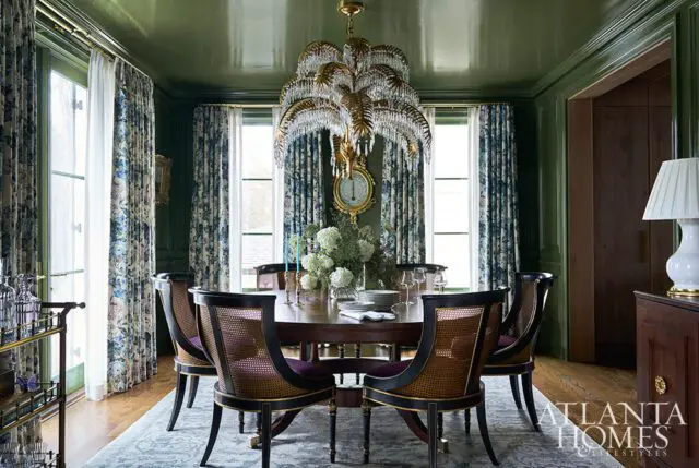 Green dining room with a round wooden table, cane-backed chairs, and a crystal chandelier.