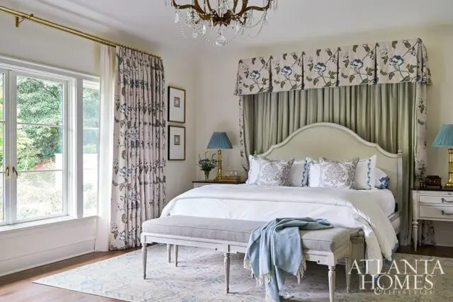 Bedroom with floral curtains, upholstered headboard, and crystal chandelier.