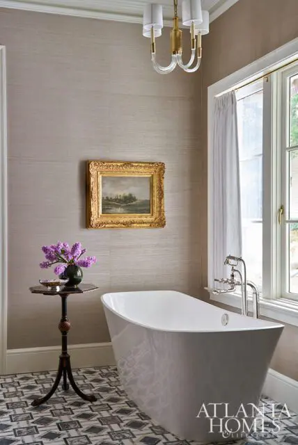 Freestanding bathtub with chrome faucet, textured taupe wallpaper, and ornate framed landscape