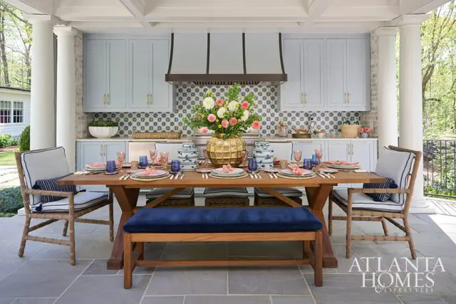 Outdoor kitchen with light blue cabinets, blue and white tile backsplash, and a wooden dining table