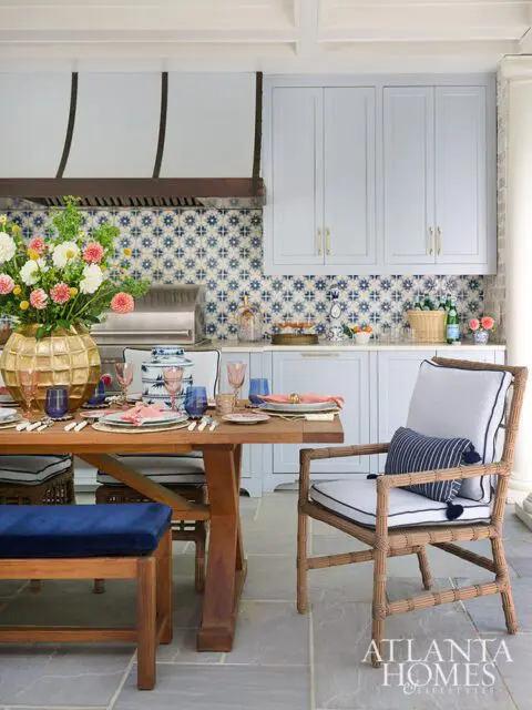Outdoor kitchen with blue tile backsplash, light blue cabinets, and a wooden dining table set for a