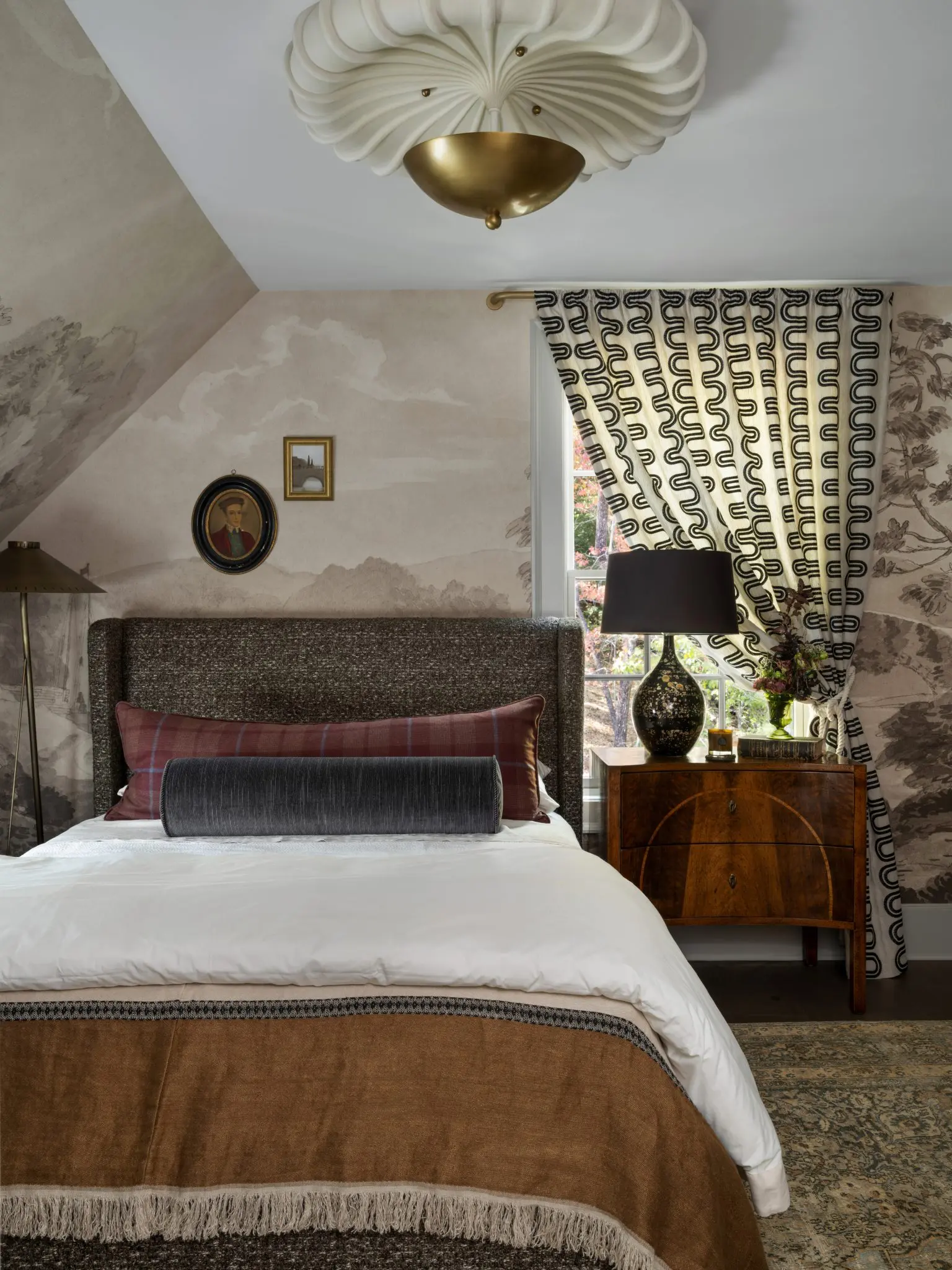 Bedroom with landscape wallpaper, upholstered headboard, and patterned curtains.