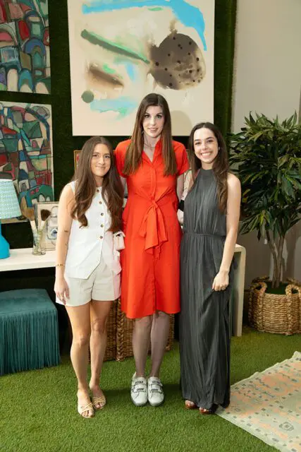 Three women posing in front of abstract art and faux grass wall.