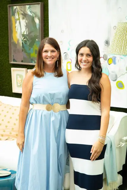 Two women smiling, one in a light blue dress, the other in a navy and white striped dress.