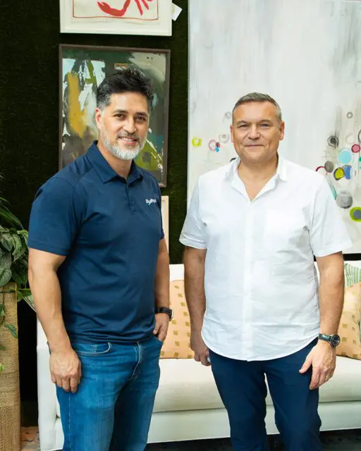 Two men standing in front of abstract art and a moss wall.