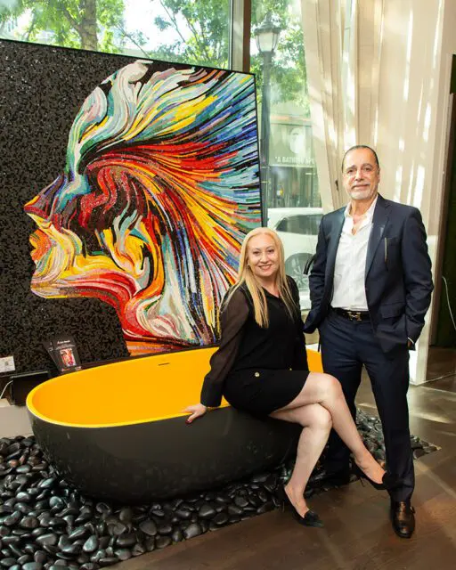 Woman and man posing by a bathtub with a colorful mosaic artwork of a profile.