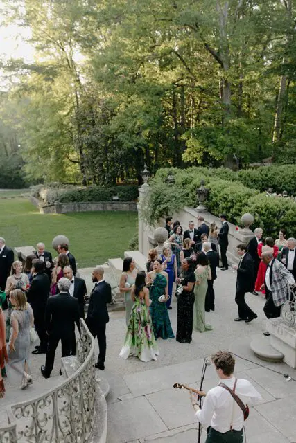 People in formal attire gathered on stone steps with a musician playing guitar.