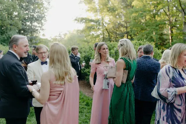 People in formal attire mingling outdoors at a garden party