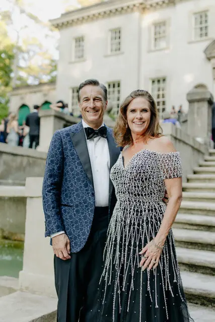 Man in patterned blue tuxedo jacket and woman in beaded black gown smiling outdoors
