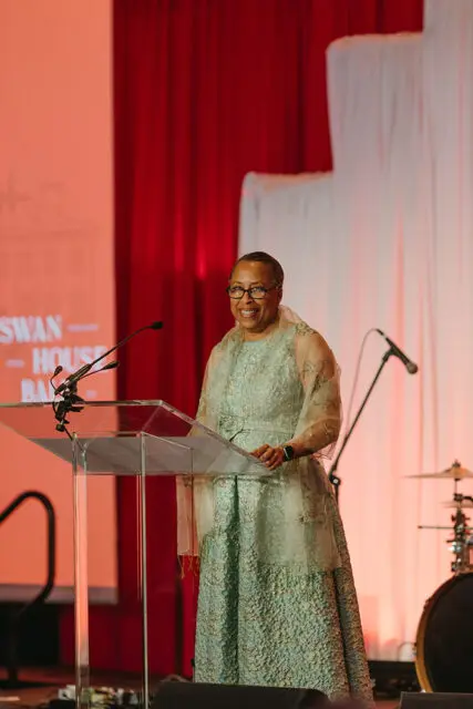 Woman in a light blue patterned dress and sheer shawl speaks at a podium.