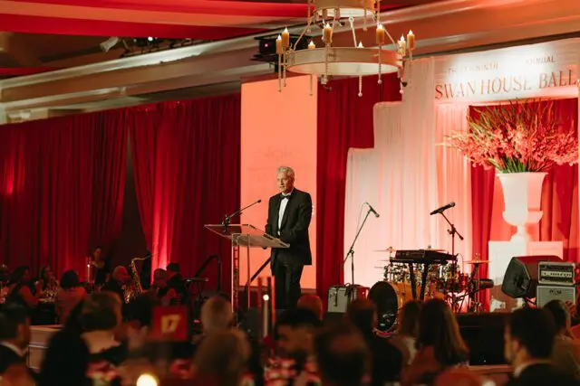 Man in tuxedo speaking at podium during Swan House Ball event