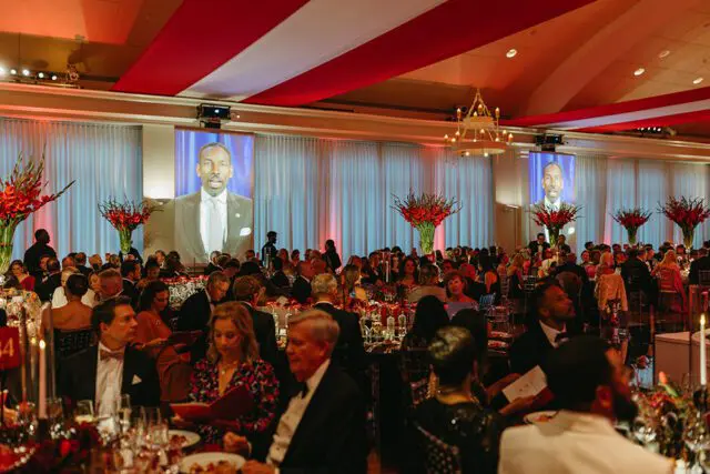 Formal dinner with screens showing a man in a suit, red and white ceiling decor