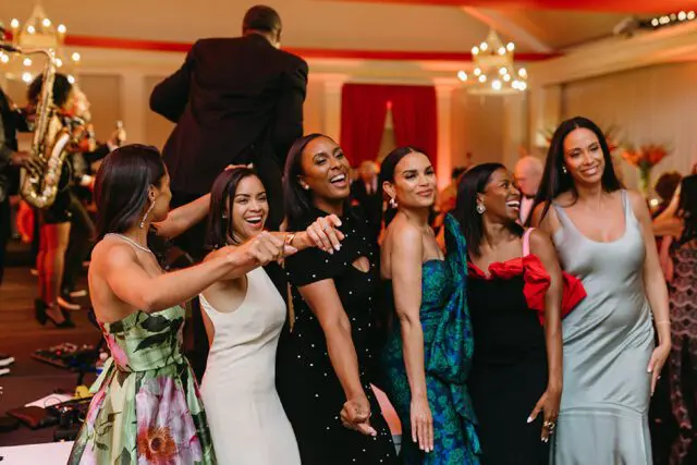 Women in formal attire dancing at a gala with a live band in the background.