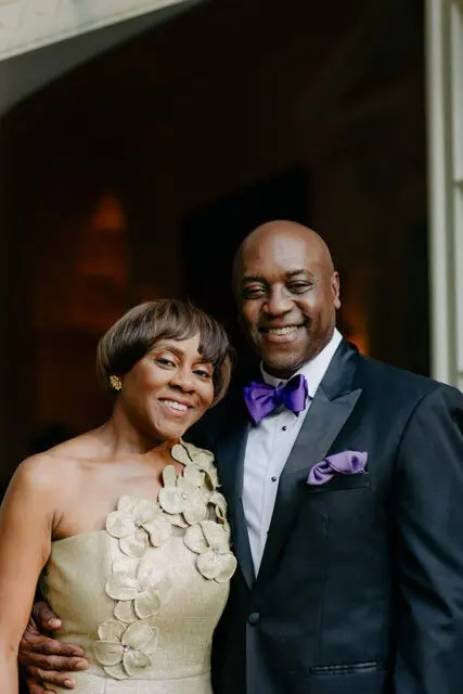 Couple smiling, woman in gold dress, man in tuxedo with purple bow tie