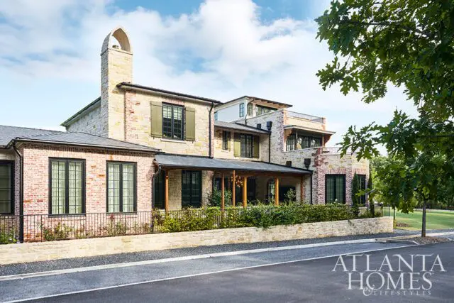 Stone and brick house with arched chimney, green shutters, and covered porch.