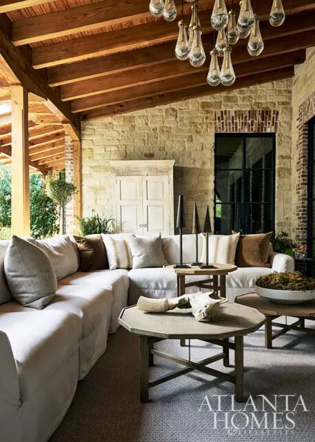 Covered patio with stone walls, wood ceiling, sectional sofa, and rustic tables.