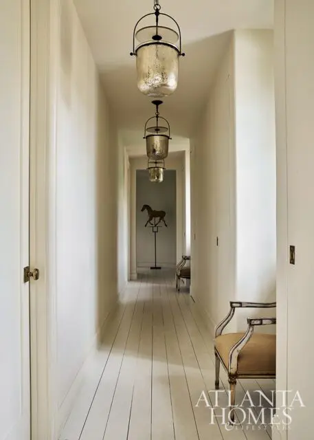 Hallway with white painted floorboards, hanging glass lanterns, and antique chairs.