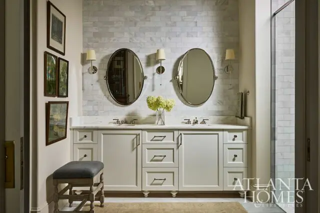 Bathroom with white vanity, marble countertop, two oval mirrors, and subway tile wall