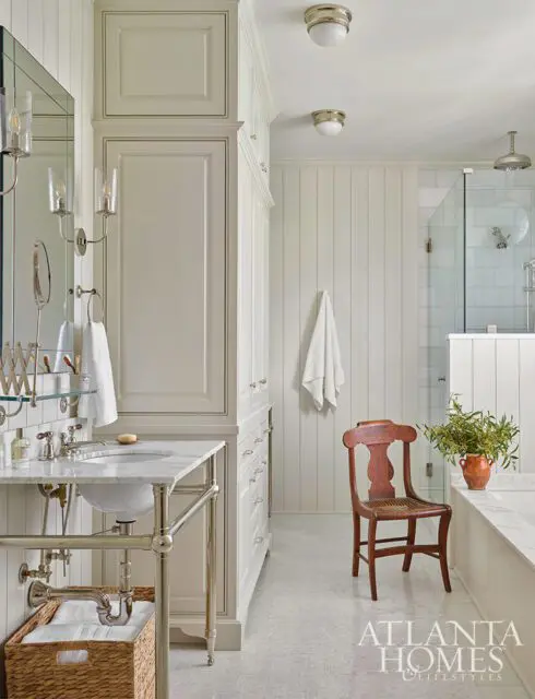 Cream bathroom with marble vanity, beadboard walls, glass shower, and wooden chair