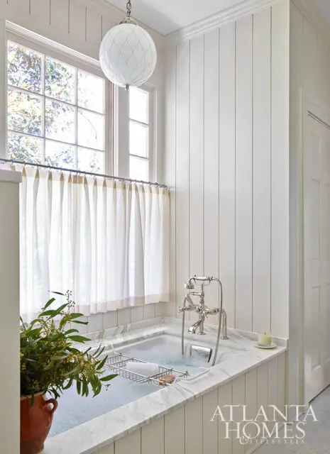 White paneled bathroom with marble tub, vintage faucet, and globe pendant light.
