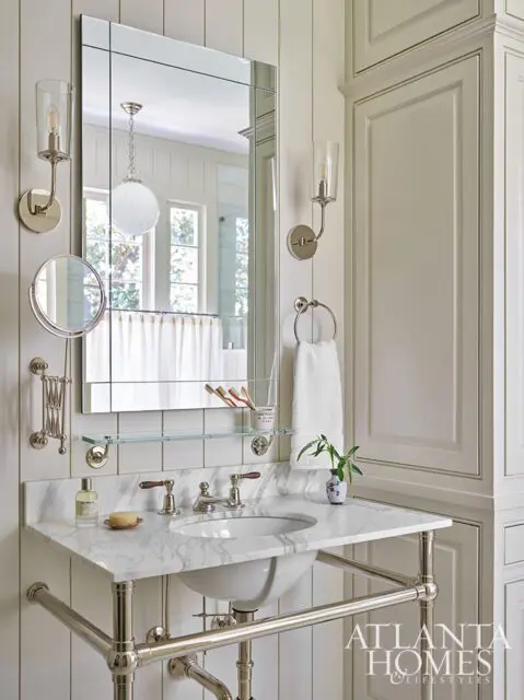 Marble vanity with nickel faucet and sink, flanked by sconces and a mirrored medicine cabinet.