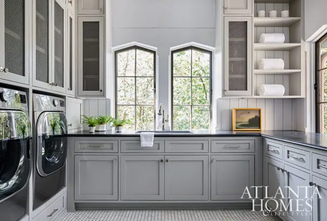 Gray laundry room with stacked washer and dryer, black countertop, and arched windows.