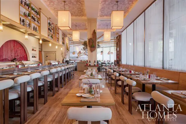 Restaurant dining room with sushi bar, wood tables, and white upholstered chairs.