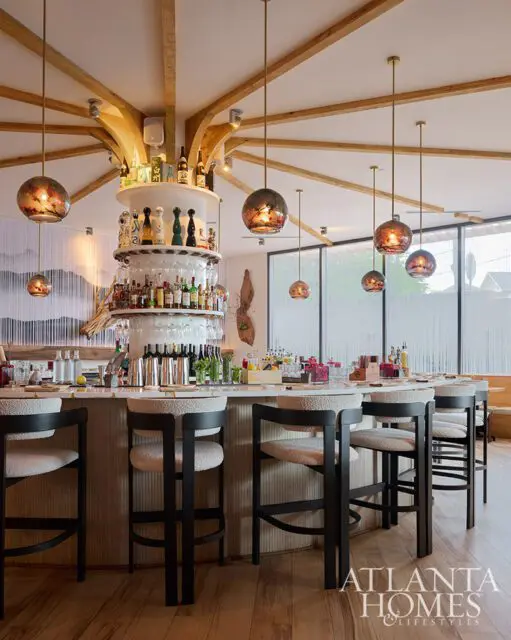 Bar with white marble counter, black stools with textured seats, and tiered bar shelves with