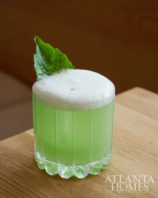 Green cocktail with foam and a basil leaf garnish in a fluted glass