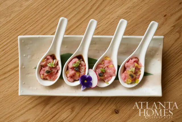 Four white spoons filled with tuna tartare topped with capers and herbs